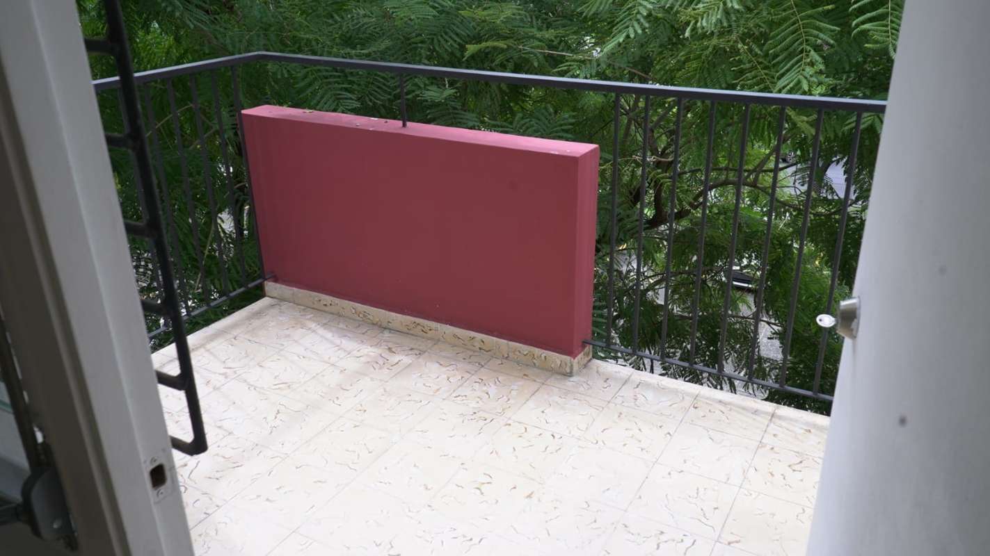 Small balcony with red wall iron railing overlooking green trees in PH Trébol Panama
