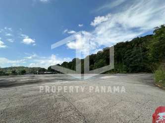 Exterior of single story blue and white building with large open paved lot and forested background in Panama