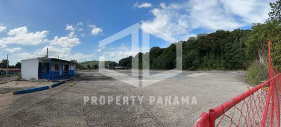 Large paved lot with small utility building and red fence bordered by forest in Rodman Panama