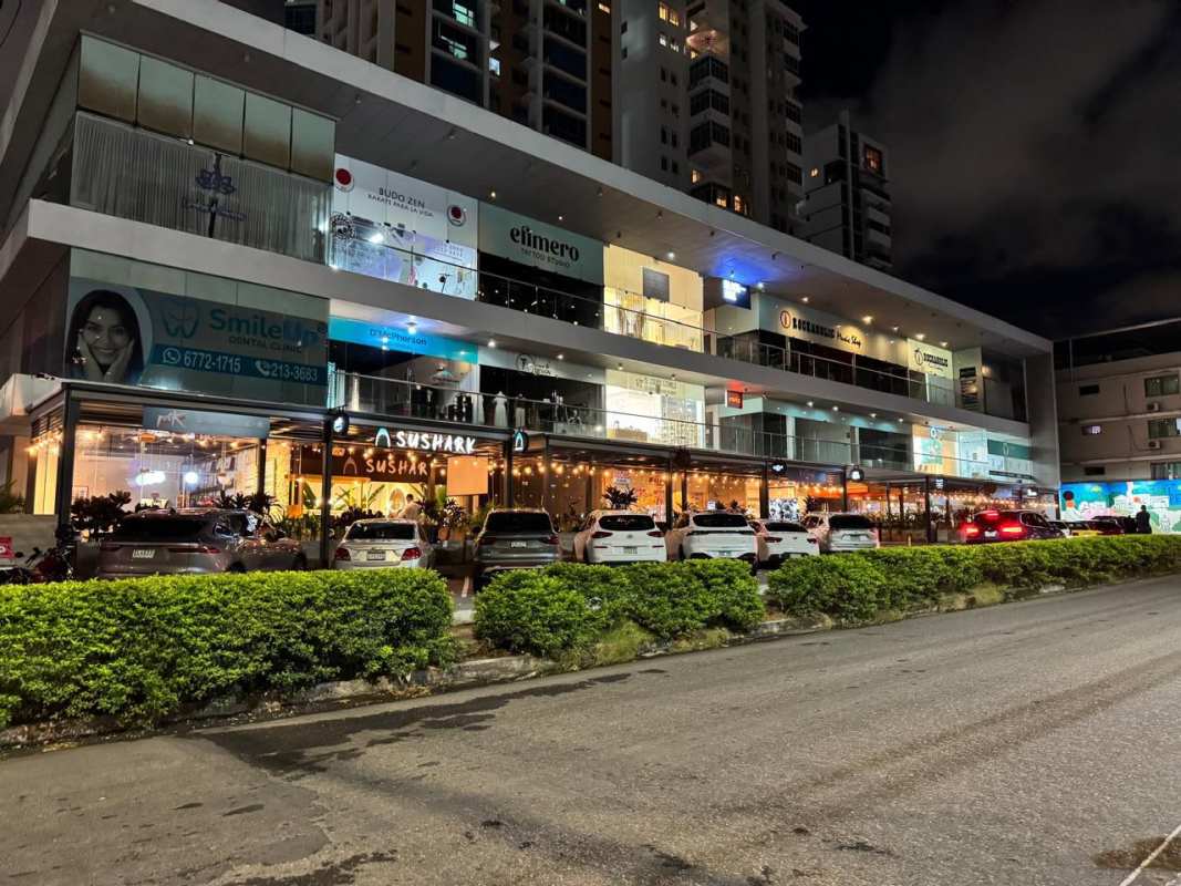 Night view of illuminated modern commercial plaza with outdoor restaurant terrace and parking on Via Porras Panama City