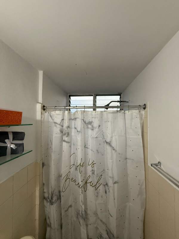 Compact bathroom with shower curtain, tiled walls, and natural ventilation at Beverly Plaza Panama