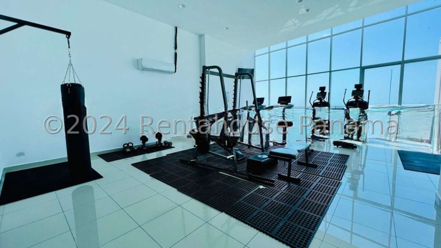 Gym room with floor-to-ceiling windows, punching bag, weights, cardio machines overlooking ocean in Serenity at the Bay