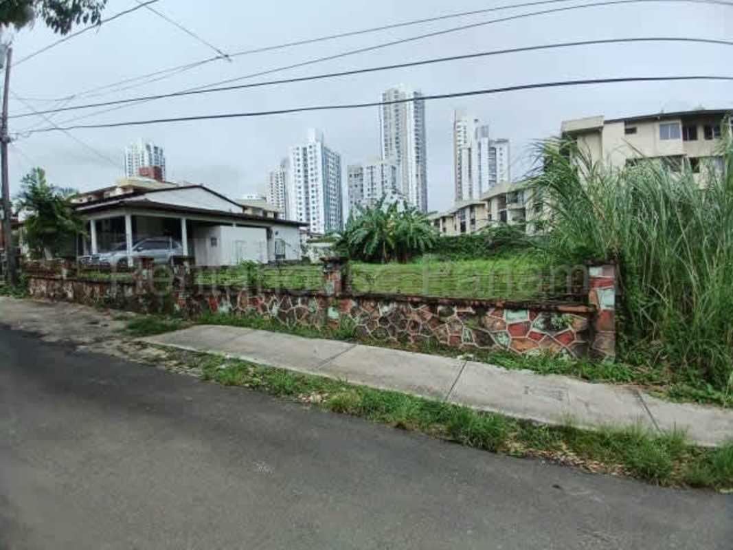 Vacant flat lot with overgrown grass and apartment buildings backdrop in Carrasquilla Panama