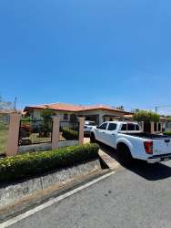 One-story fenced house with terracotta tiled roof, driveway, garden and pickup trucks Boquete area