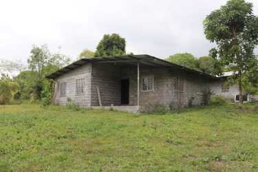 Exterior of unfinished concrete house with metal roof and large open yard with trees Boquerón Panama