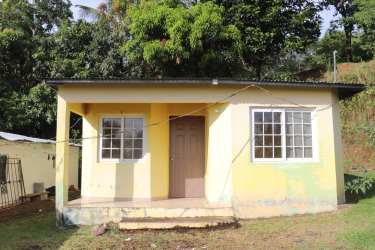 Side view of small yellow house with metal roof and wide grassy yard in Arraiján Panama