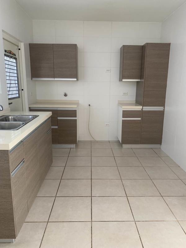 Bright kitchen with white tiled walls, brown cabinets and double sink Brisas del Golf Panama