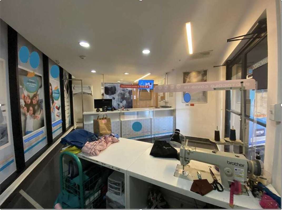 Modern commercial reception with acrylic COVID-19 barrier, sewing table and advertising posters inside Panama City laundry tailoring shop