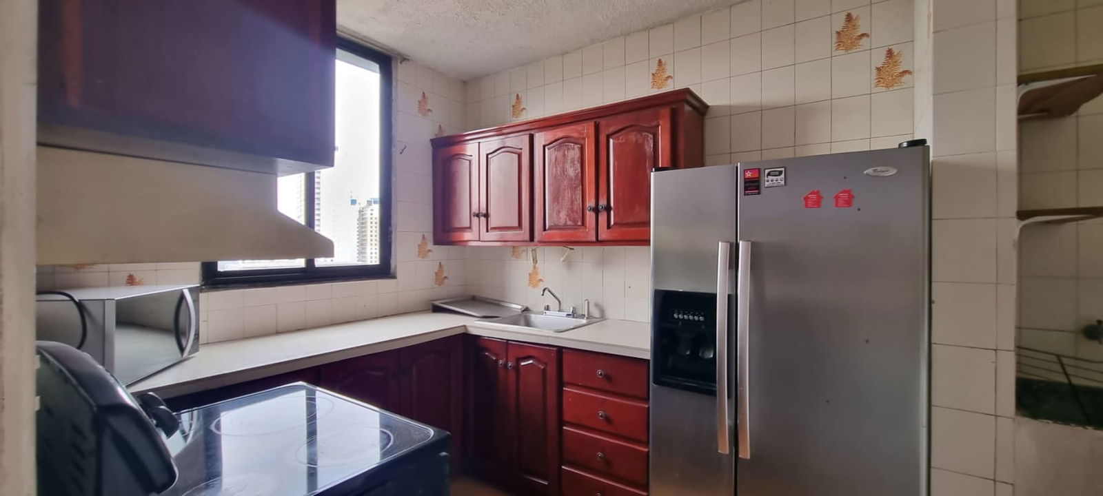 Bright kitchen with wooden cabinets, electric stove, microwave, and city view window in PH Park Loft