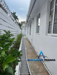 Exterior walkway beside white-walled home with garden and security fence Panama Pacifico