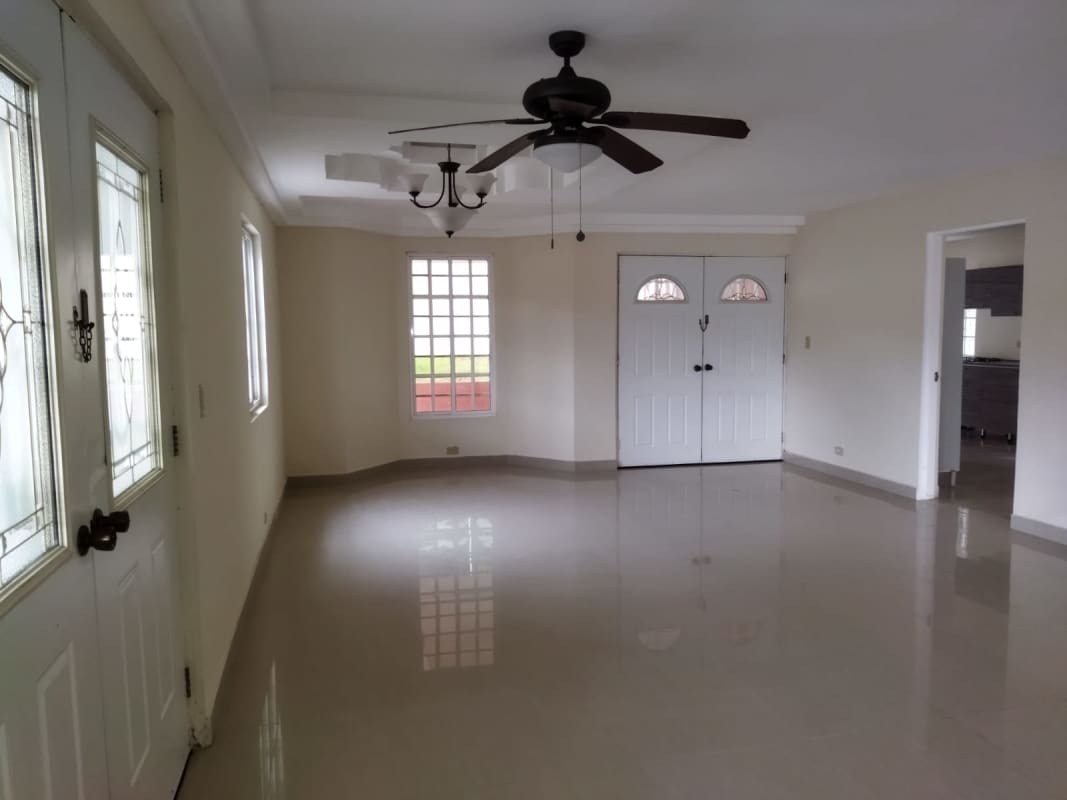 Spacious empty living room with polished tile floor, large windows and ceiling fan in Las Cumbres Panama house