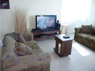 Living room with flat-screen TV green sofa tiled floors in Playa Blanca Founders I condo Panama