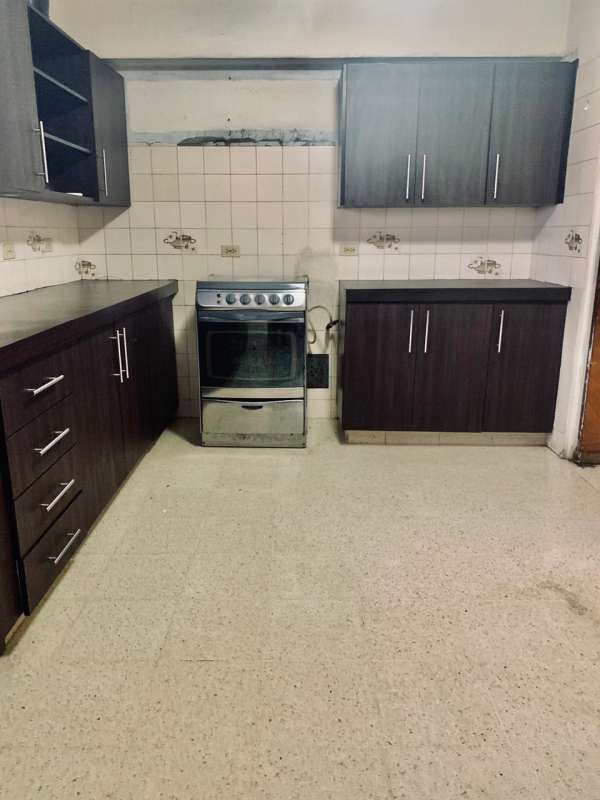 Shared kitchen with dark wood cabinets, stove, overhead cabinets at PH El Carmen 55