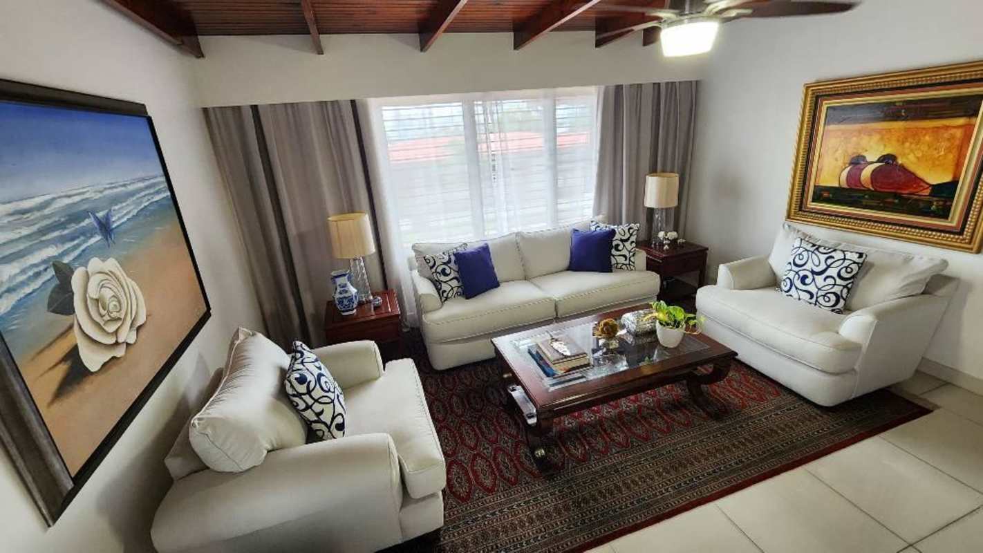 Living room with white sofas, exposed wood beams, large window, ceiling fan in Betania Panama