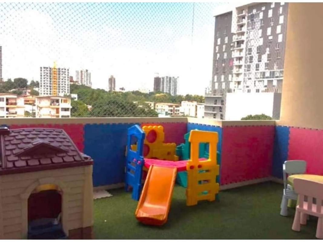 Balcony with children's playground, colorful equipment, artificial grass overlooking Panama city skyline