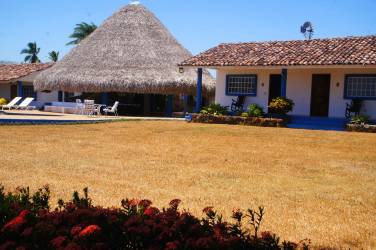 Covered thatched outdoor living space with bar, lounge, hammocks overlooking gardens
