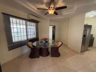 Open dining room with round glass table, wicker chairs, ceiling fan and natural light in Herrera Panama