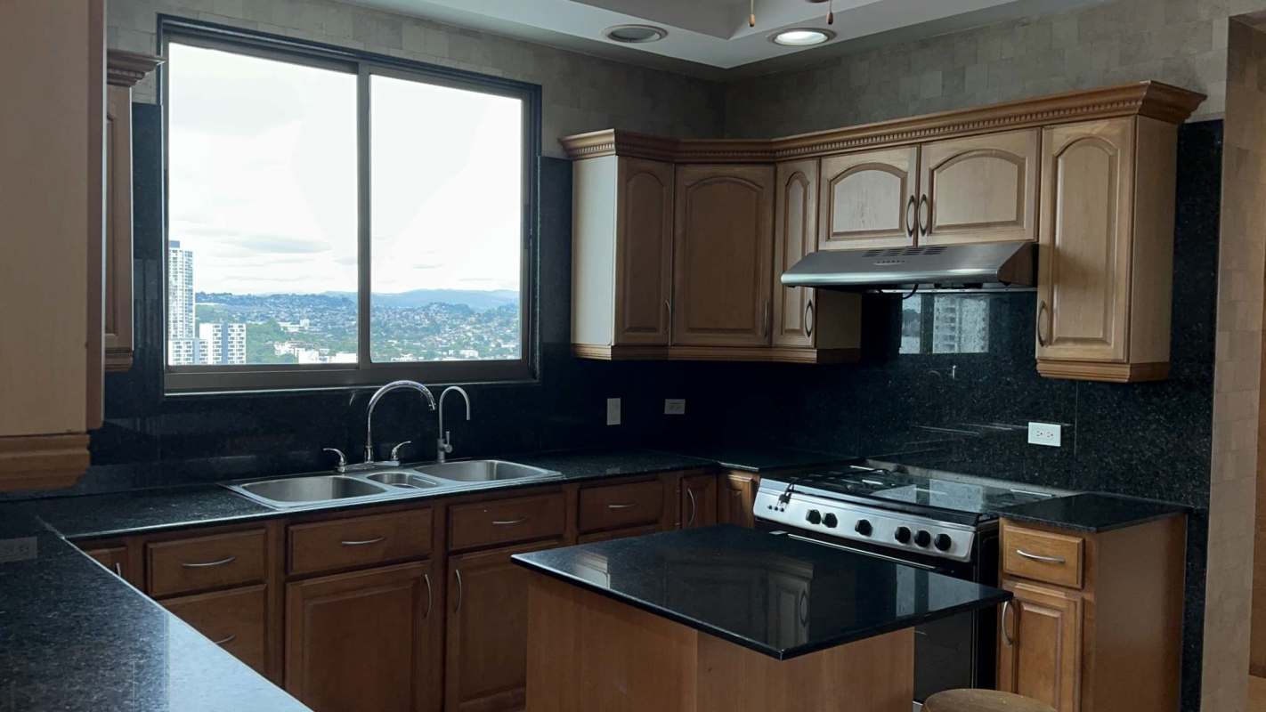 Traditional kitchen with wood cabinetry, granite counters and panoramic window views in luxury penthouse Panama City