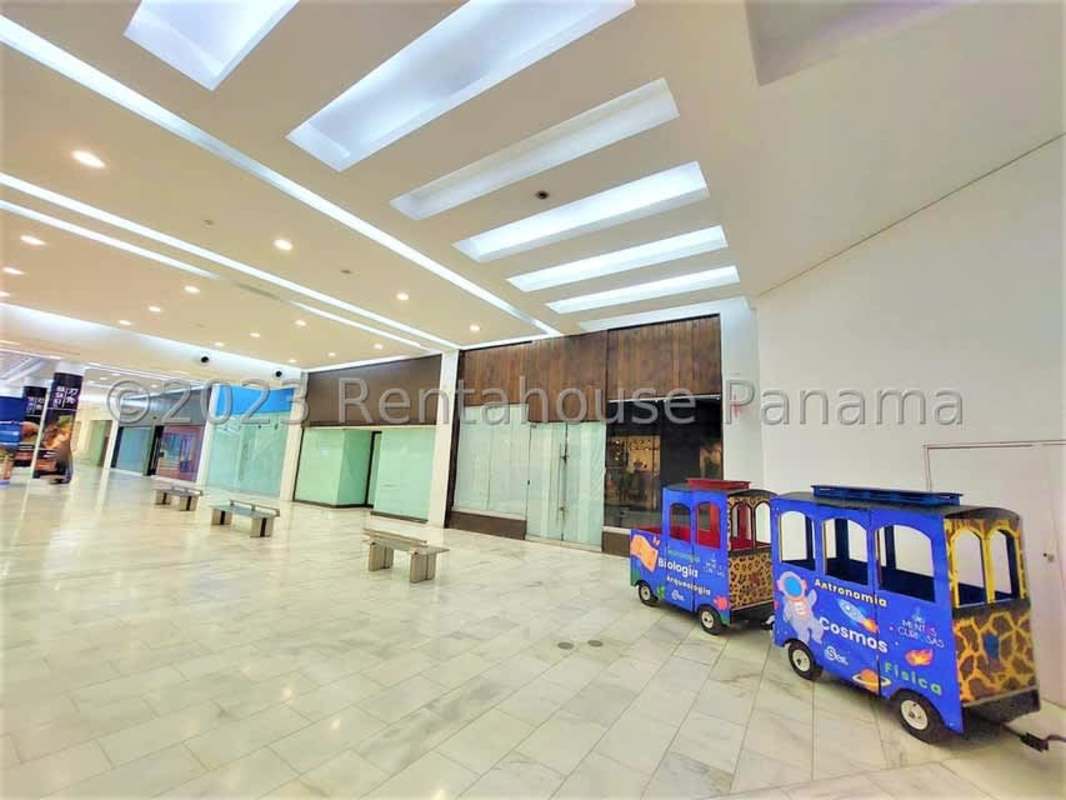 Shopping mall corridor with glass storefronts, benches and children play train at Albrook Mall Panama