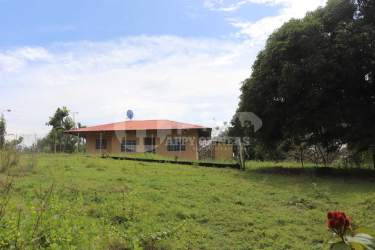 Small farmhouse with red metal roof and garden lawn on large rural land in Panama