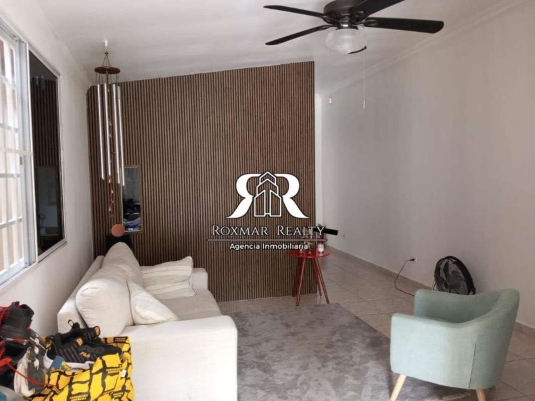 Living room with wooden accent wall cream sofa area rug ceiling fan Brisas del Golf