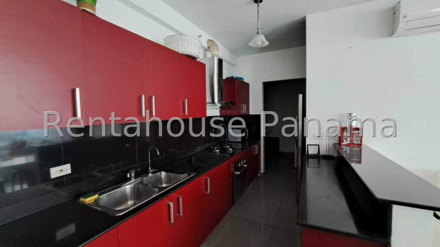 Modern apartment kitchen with red cabinetry, black countertops and double sink in PH Quartier 74 Panama