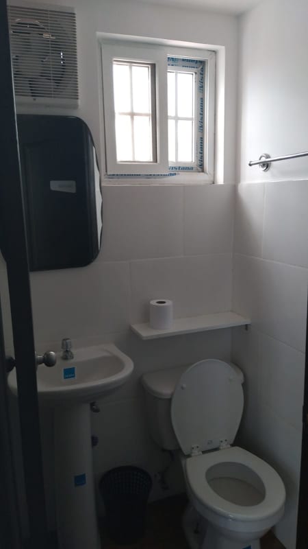 Small white minimalist bathroom with pedestal sink and toilet in rented office Panama City
