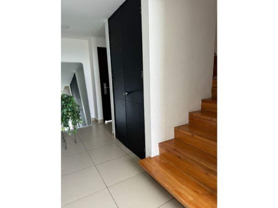 Modern hallway with wooden staircase, beige tiles and black accents in Costa Sur Village Panama