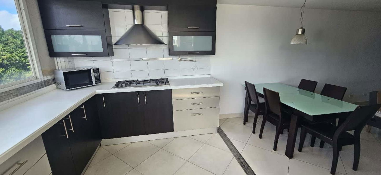 Open kitchen with black cabinetry, stainless steel hood, glass dining table in PH San Miguelito Suites Panama