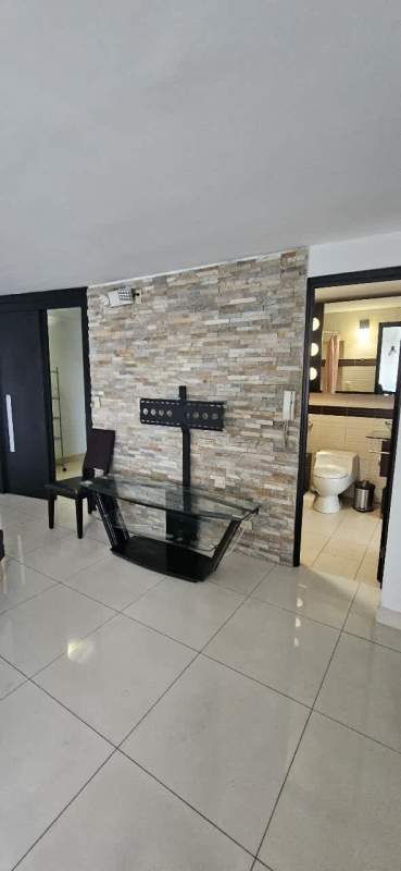 Living room with stone accent wall, glass TV stand PH San Miguelito Suites Panama