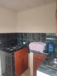 Small kitchen area with wooden cabinets, black tile backsplash, gas stove, microwave space