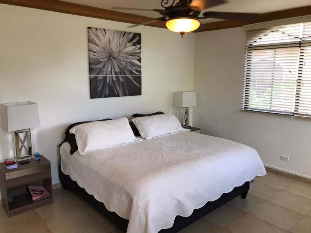 Master bedroom with king bed, nightstands, lamps, ceiling fan, window with garden view at Clayton Village