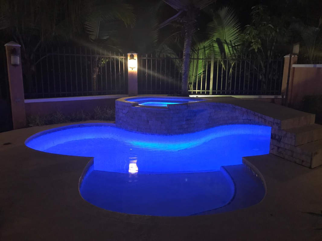 Private illuminated swimming pool with elevated Jacuzzi surrounded by garden in Clayton Village