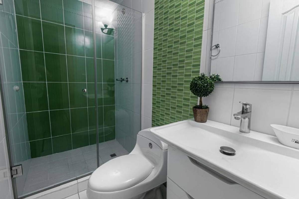 Remodeled bathroom with glass-enclosed shower, green accent tiles and modern sink in Panama City