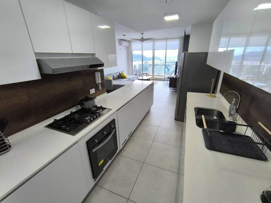 Open kitchen with white cabinets, stove, living area with city view balcony PH Van Gogh Panama City