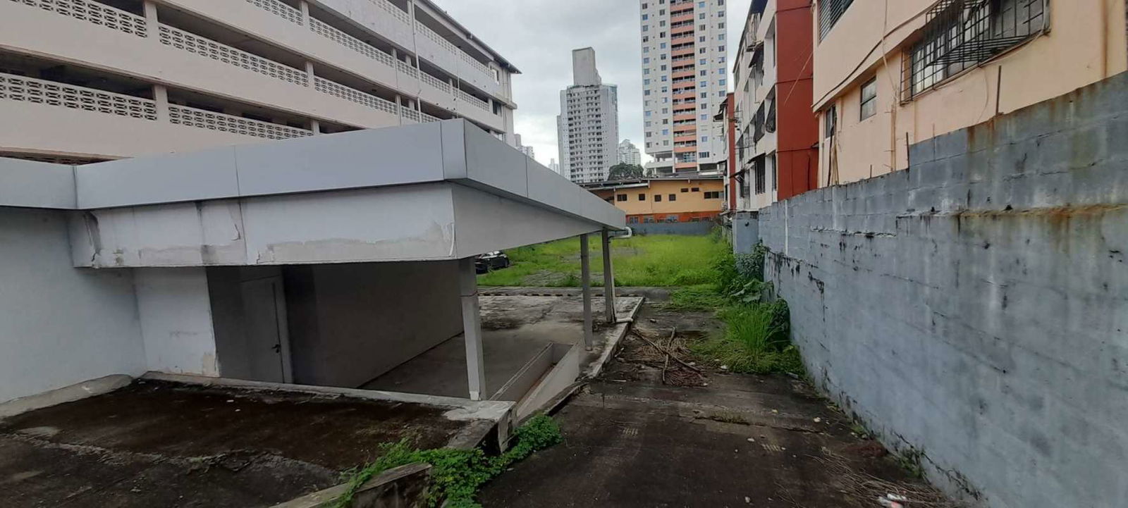 Vacant urban lot with overgrown grass and nearby residential buildings Via Porras Panama