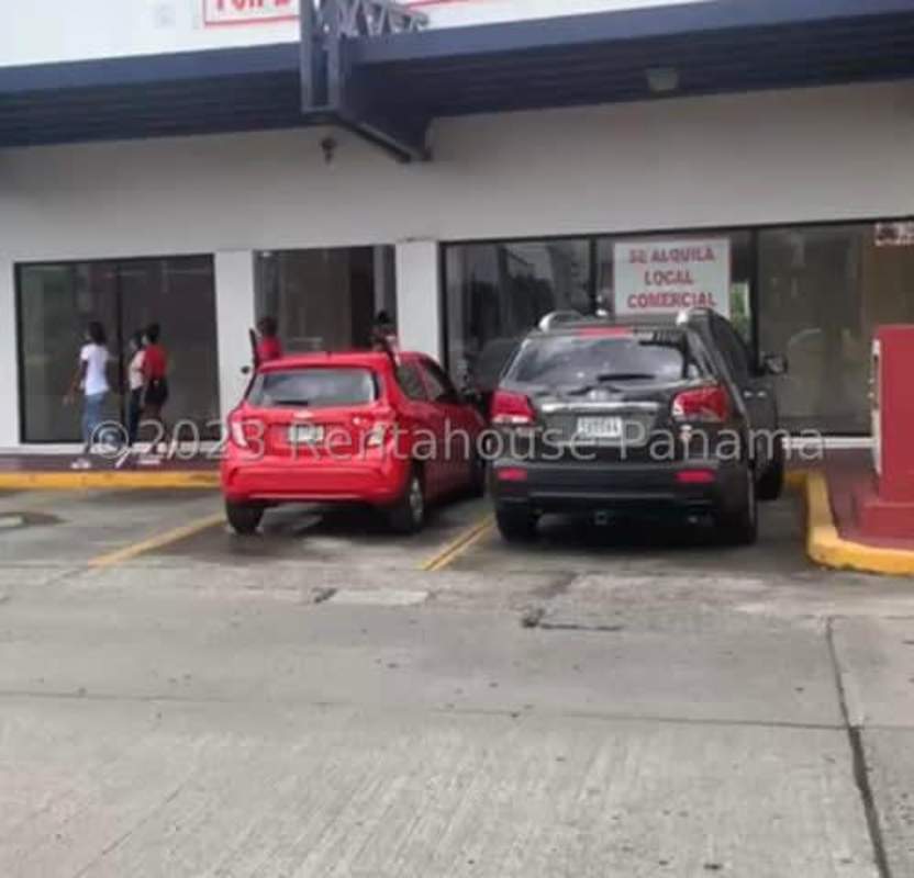 Busy commercial avenue with cars, billboard and green spaces near Los Pueblos Panama