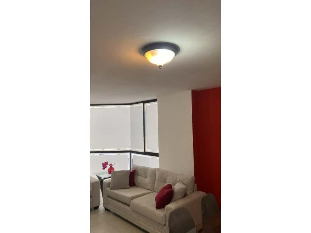 Living area with large corner windows, beige sectional, decorative cushions in Paitilla apartment