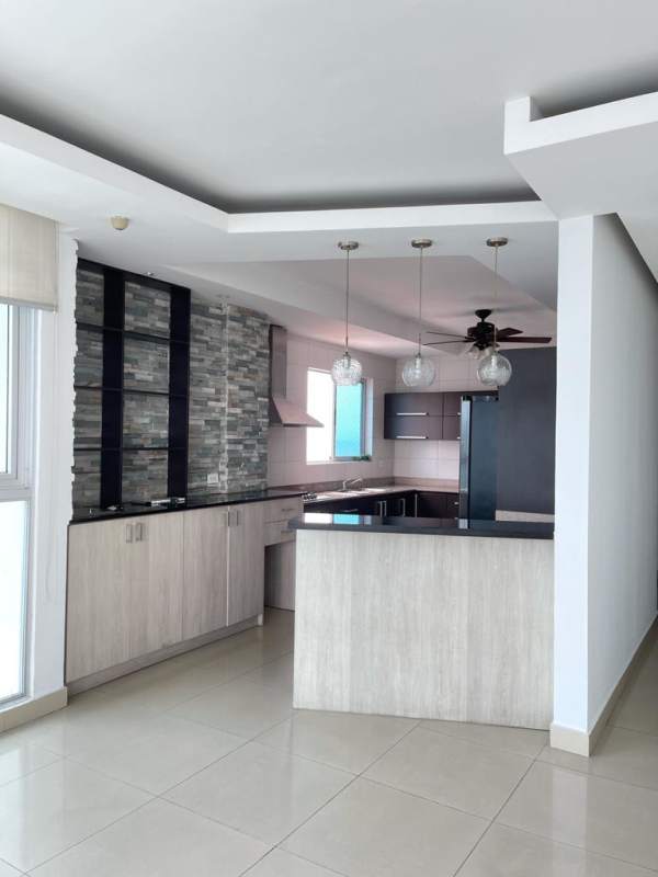 Open-plan modern kitchen with island, light wood cabinetry and black countertops in PH The View Coco del Mar