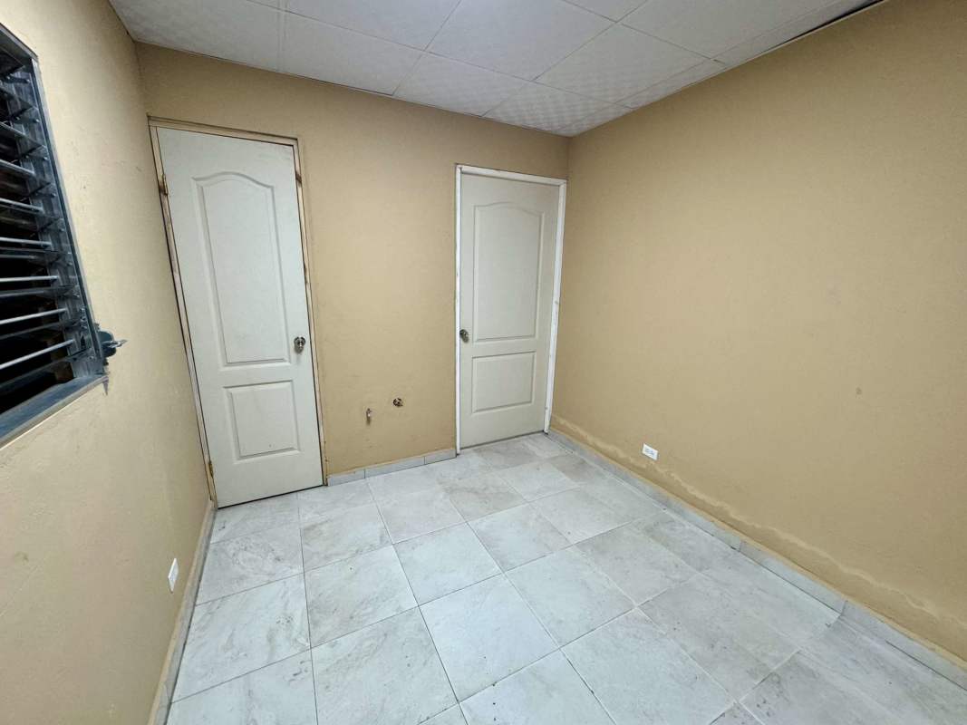 Small bedroom or office space with beige walls, tile floor, barred window in commercial property Parque Lefevre Panama
