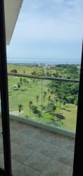 View from balcony with glass railing overlooking green golf course and Pacific Ocean