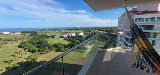 View from balcony with glass railing overlooking lush golf course and Pacific Ocean