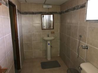 Simple bathroom with beige tiled walls, pedestal sink, mirror, and handheld shower in Penonomé residential property