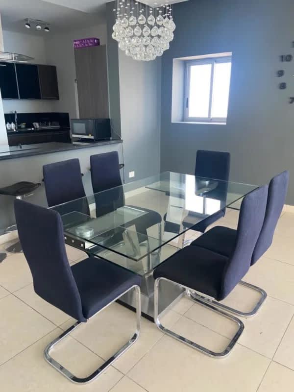 Dining area with glass table, navy chairs, chandelier and open kitchen in Punta Paitilla condo