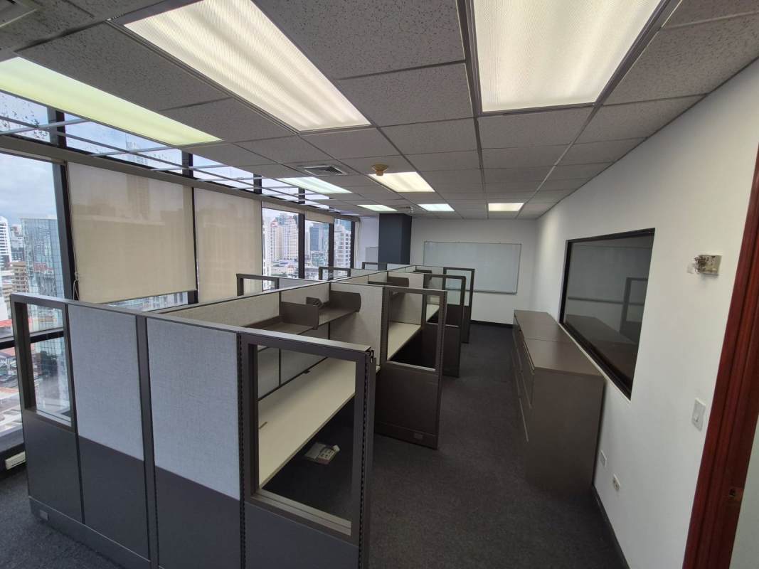 Office workspace divided with glass walls, fluorescent lighting, city view windows inside Banco General Building Calle 50