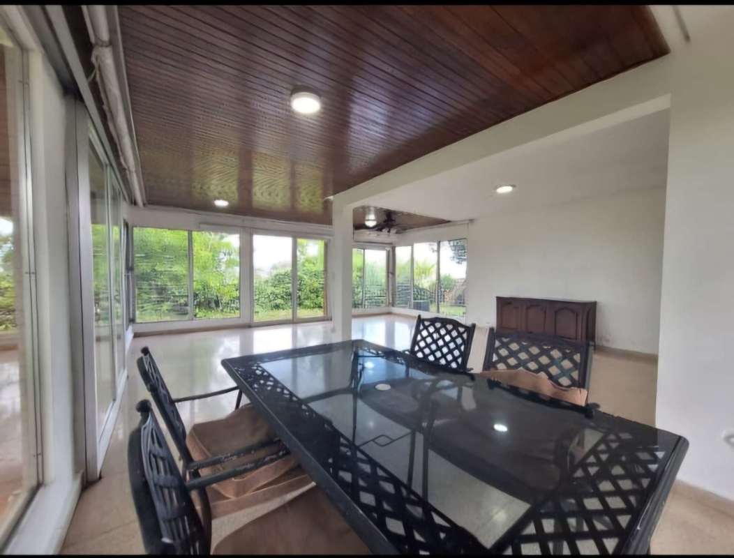 Modern enclosed patio with wood ceiling, large windows, dining area and garden views in Villa de las Fuentes Panama