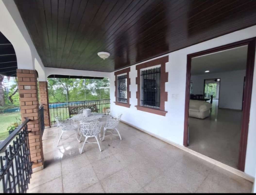Backyard covered patio with iron railing, outdoor furniture, tiled floor and garden view in Villa de las Fuentes Panama