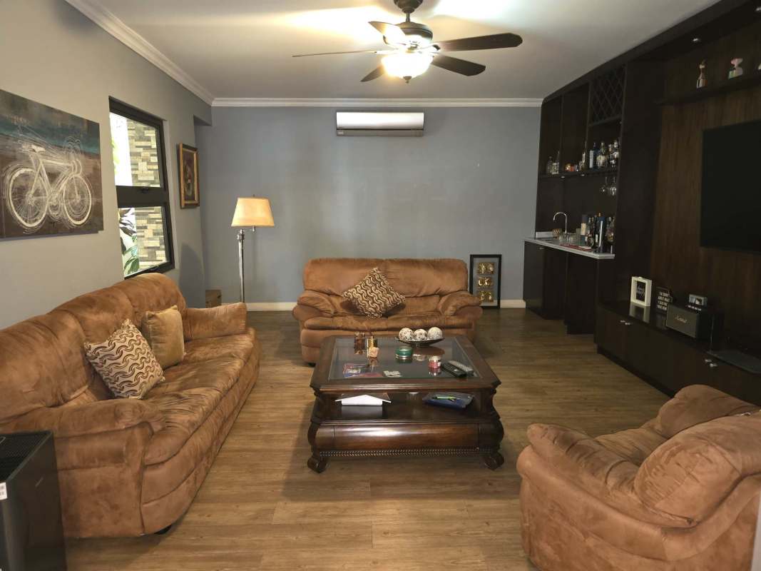 Spacious living room with wood flooring, suede sofas, built-in wall unit, ceiling fan, wet bar in Costa del Este Panama house