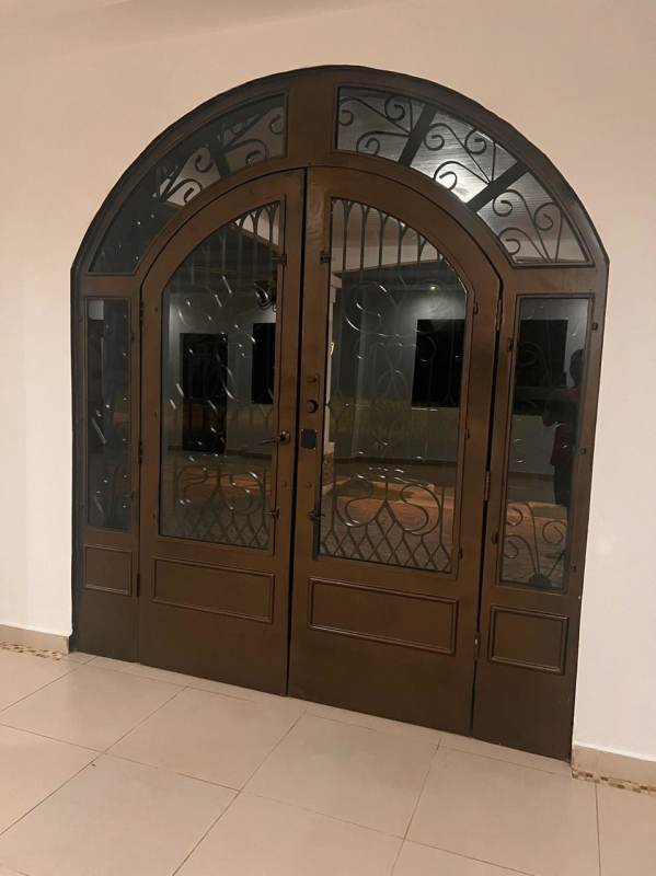 Arched brown double doors with wrought iron accents inside tiled entry hall in Llanos de Curundu residence Panama City
