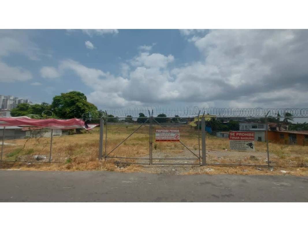 Vacant fenced lot with metal fence, barbed wire, and urban environment
